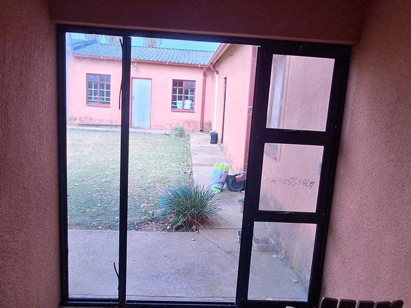 A covered patio area looking out onto a rear garden and secondary building structure, featuring a metal-framed glass door and textured wall finishes.