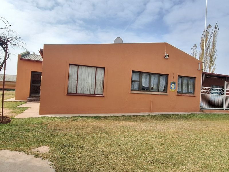 Front elevation of a single-story small holding dwelling featuring a painted exterior, aluminum window frames, and an attached security gate.