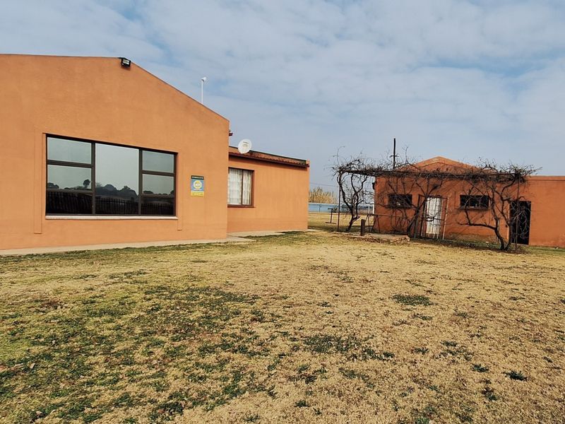 Rear view of the property showing two separate structures, large windows, and a spacious garden area with a pergola.