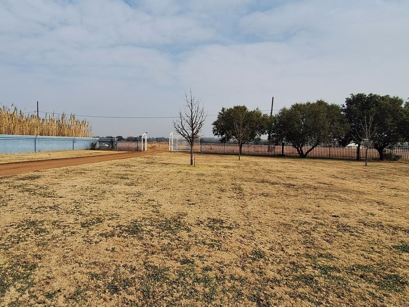 Expansive open garden area featuring perimeter fencing, a boundary wall, and gated access on a small holding property.