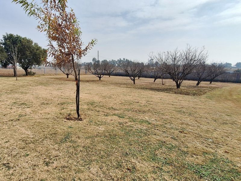 A spacious, open garden area featuring established trees and secure perimeter fencing, offering potential for landscaping and outdoor development.