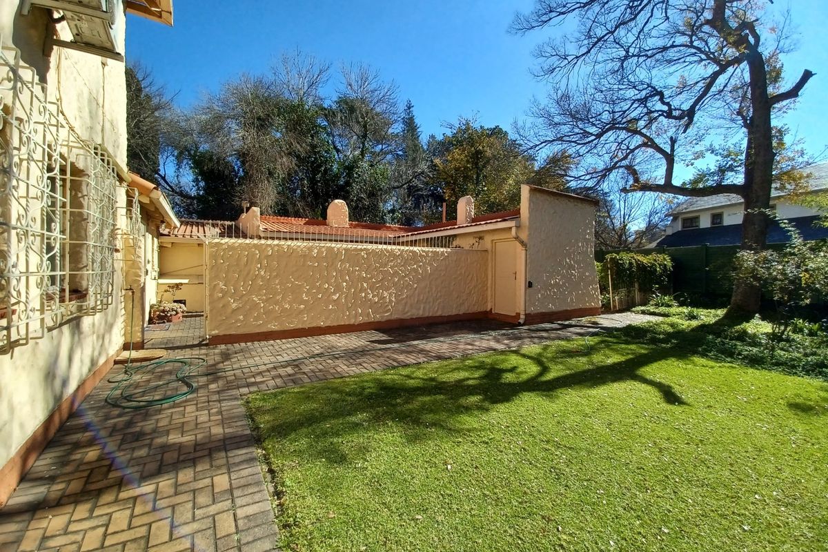 A spacious rear garden featuring a paved patio area, a well-maintained lawn, and secure boundary walls.