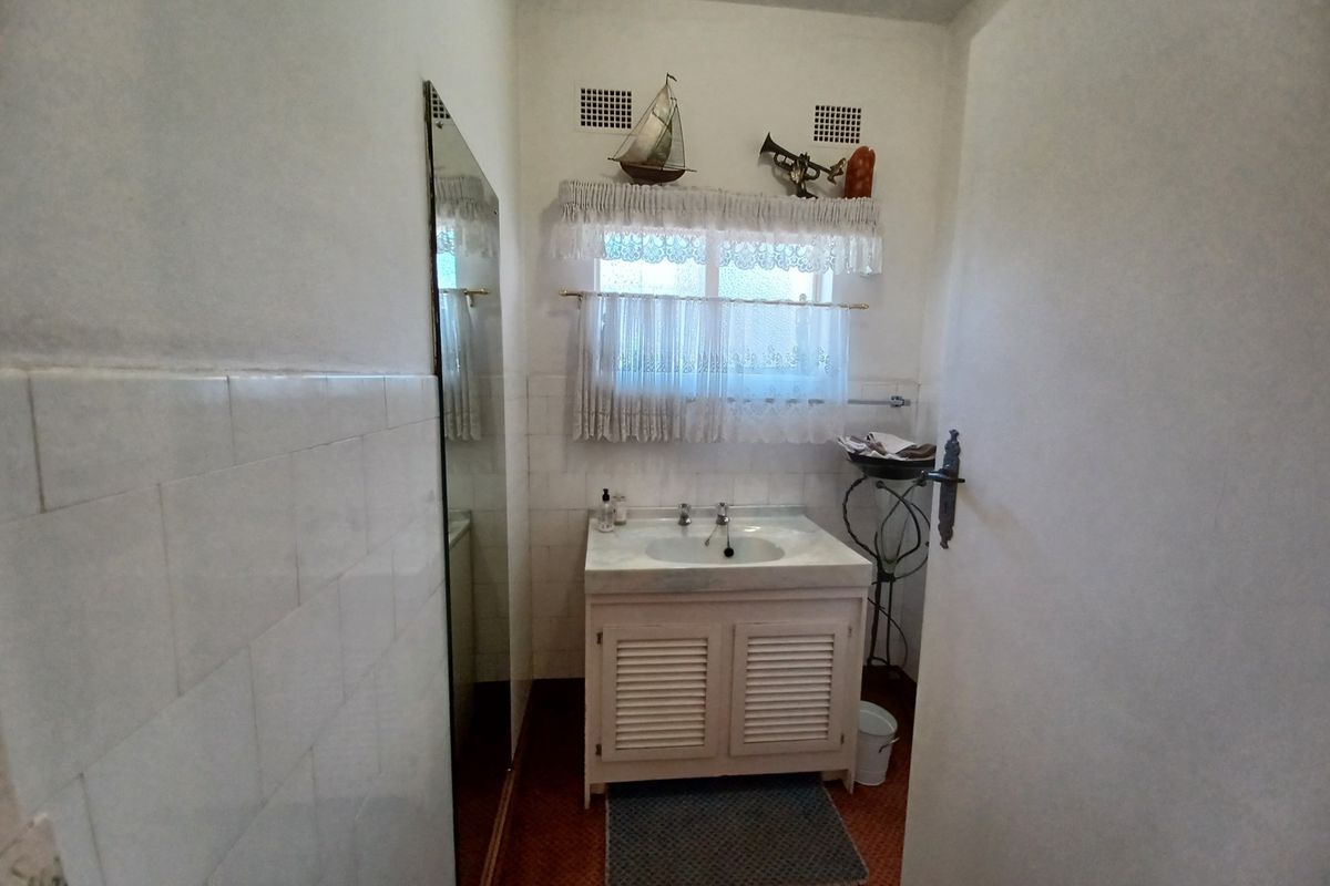 A compact bathroom featuring a vanity cabinet with a ceramic basin, wall-mounted mirror, and tiled wall finishes.