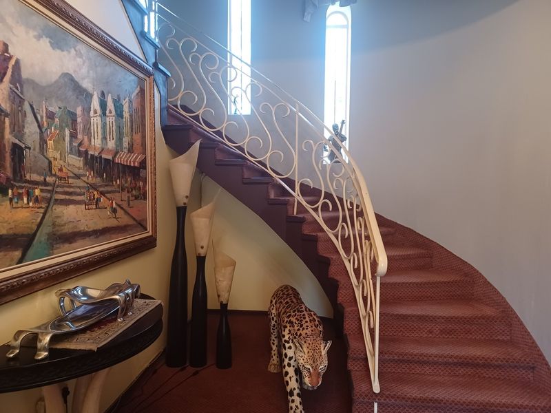 A grand curved staircase featuring a decorative wrought iron balustrade and carpeted steps, illuminated by tall arched windows in the entrance hallway.