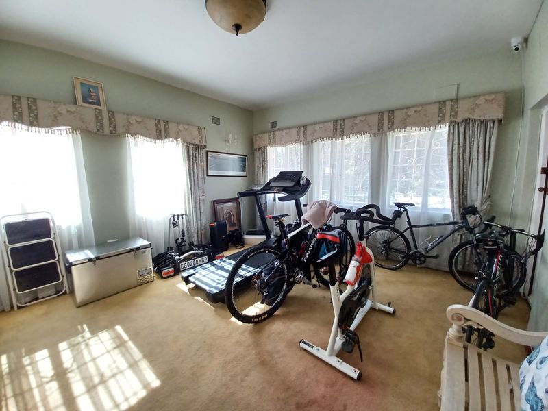 A spacious room currently utilized as a home gym, featuring large windows with security gates and carpeted flooring.