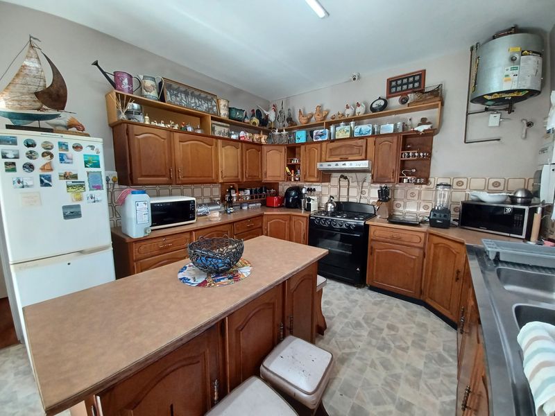 A traditional kitchen featuring wooden cabinetry, laminate countertops, a central island, and a tiled backsplash, offering potential for a modern renovation.