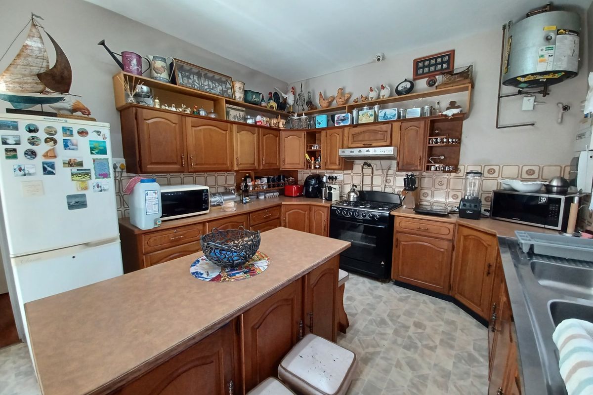 A traditional kitchen featuring wooden cabinetry, laminate countertops, a central island, and a tiled backsplash, offering potential for a modern renovation.