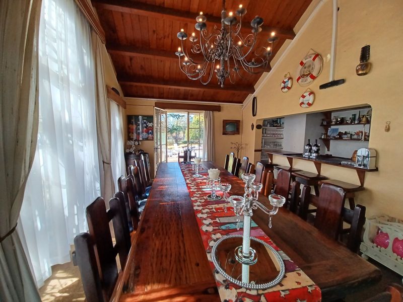 Spacious dining room featuring an exposed timber ceiling, a built-in bar area, and large windows providing natural light and access to the garden.