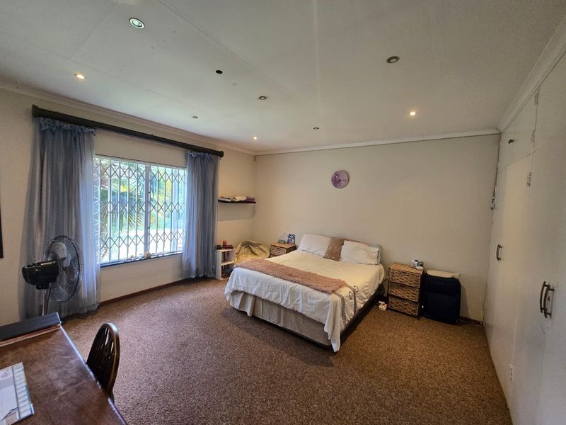 Spacious bedroom featuring carpeted flooring, built-in cupboards, and large windows fitted with security burglar bars.