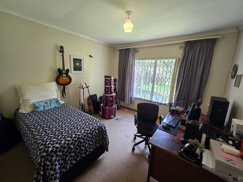 A standard bedroom featuring a large window with a fitted security gate and neutral wall finishes, offering a functional space for rest or study.