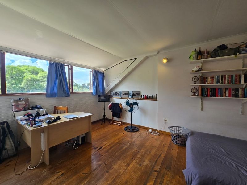 A bedroom featuring hardwood flooring, a sloped ceiling, and large windows providing natural light and garden views.