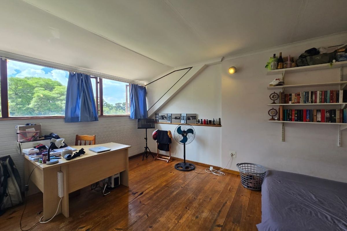 A bedroom featuring hardwood flooring, a sloped ceiling, and large windows providing natural light and garden views.