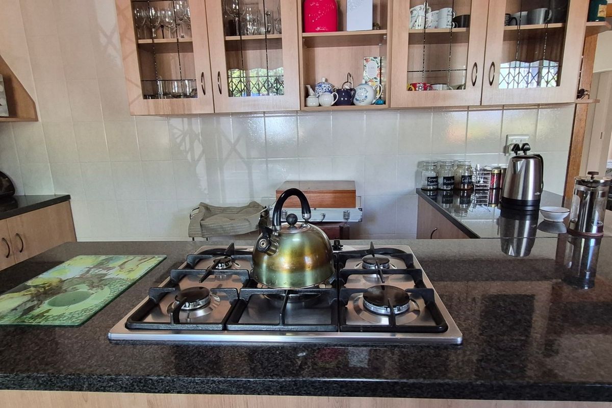A functional kitchen featuring dark granite countertops, a built-in gas hob, and ample wooden cabinetry with glass-fronted display sections.