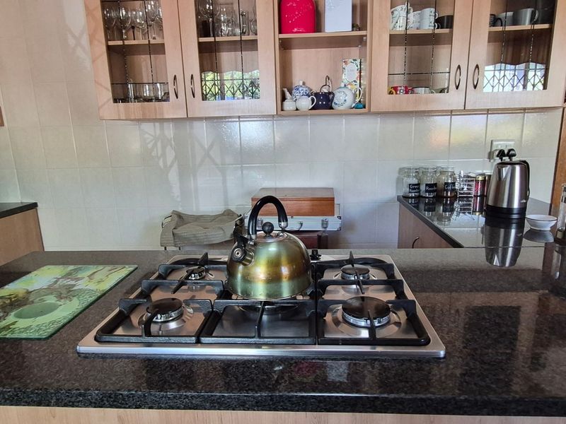 A functional kitchen featuring dark granite countertops, a built-in gas hob, and ample wooden cabinetry with glass-fronted display sections.