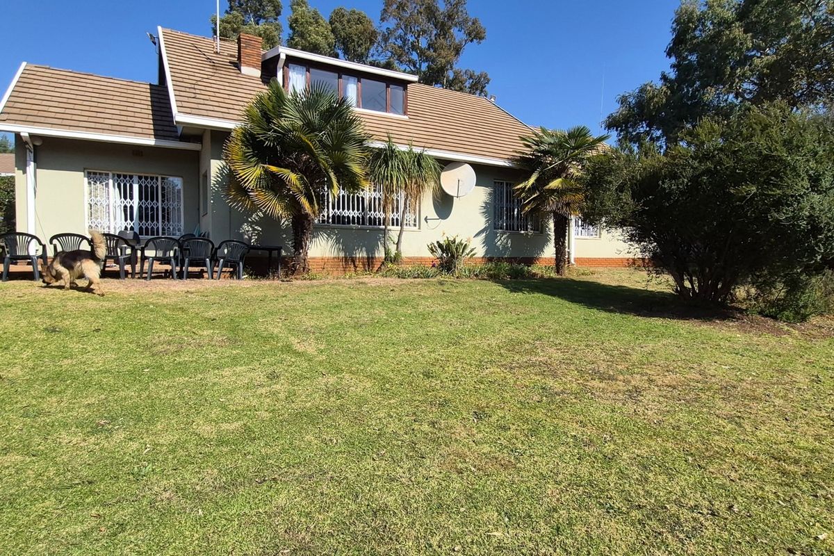 Rear view of the property featuring a tiled roof, security gates on windows, and a paved patio area overlooking a spacious garden.