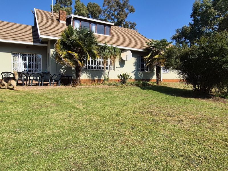 Rear view of the property featuring a tiled roof, security gates on windows, and a paved patio area overlooking a spacious garden.
