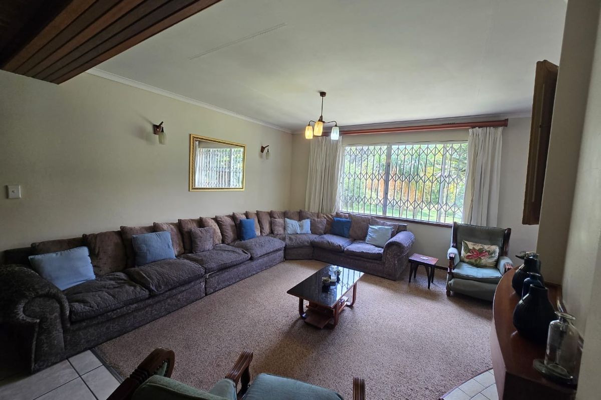 Spacious living room featuring large windows with security bars, neutral wall finishes, and a combination of carpeted and tiled flooring.