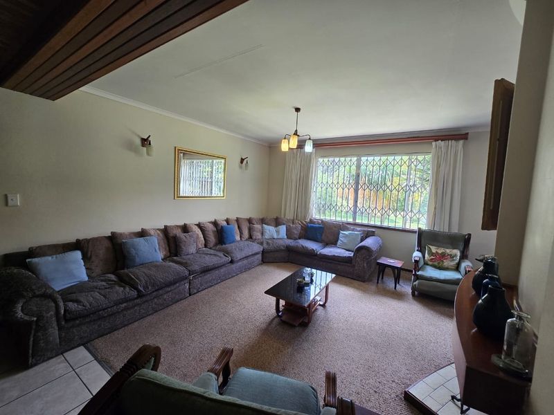 Spacious living room featuring large windows with security bars, neutral wall finishes, and a combination of carpeted and tiled flooring.