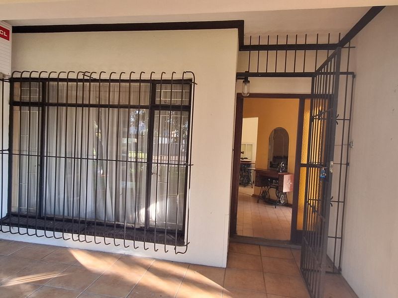 A covered patio area featuring tiled flooring, security bars on the window, and a wall-mounted air conditioning unit.