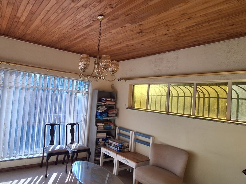 Living room featuring a timber tongue and groove ceiling, brass chandelier, and windows fitted with security bars and vertical blinds.