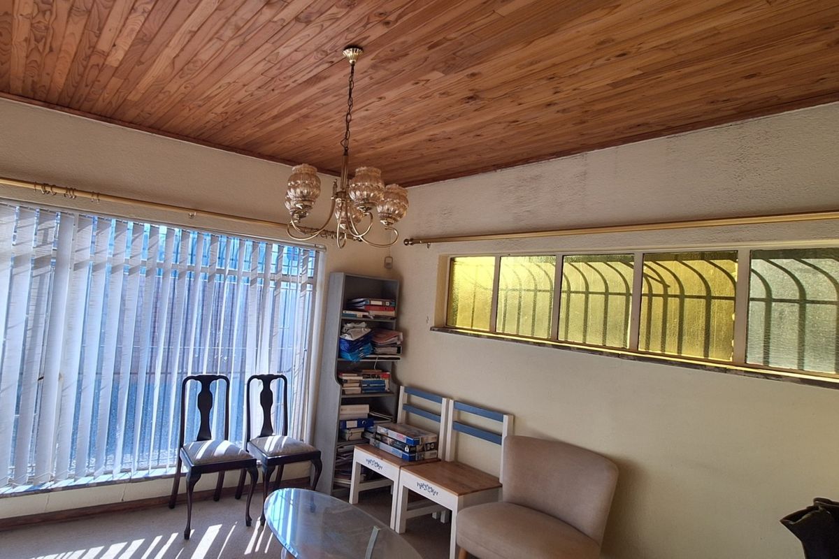 Living room featuring a timber tongue and groove ceiling, brass chandelier, and windows fitted with security bars and vertical blinds.