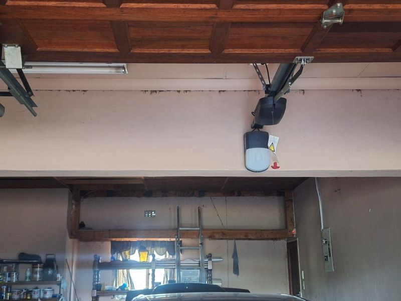 A functional garage space featuring an automatic door opener, exposed timber ceiling beams, and visible structural elements requiring maintenance and cosmetic updates.