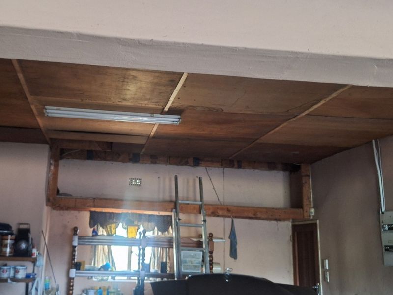 A garage space featuring an exposed timber ceiling, structural beams, and a wall-mounted electrical distribution board, requiring maintenance and finishing.