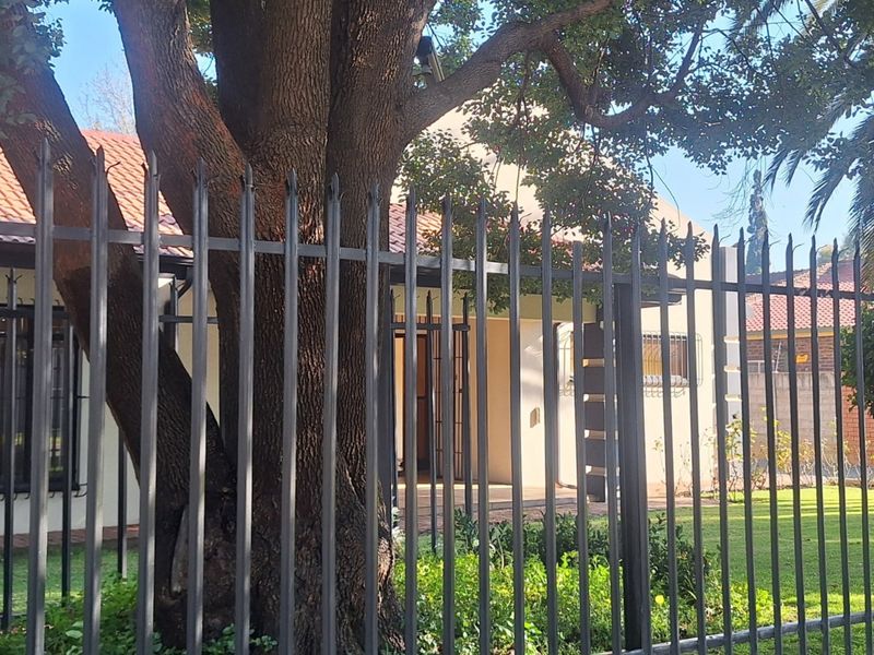 Front view of the property featuring a tiled roof, security fencing, and established trees in the front garden area.