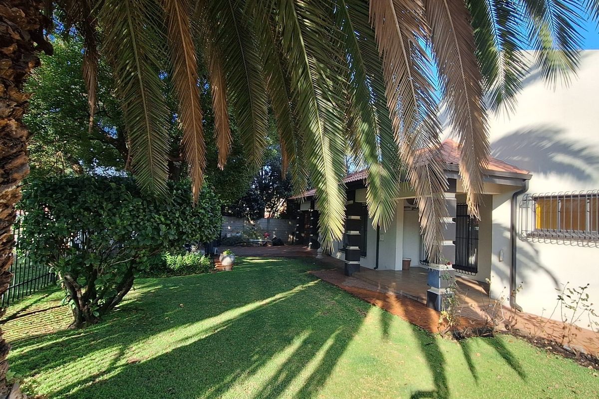 A view of the rear garden featuring a covered patio area, established palm tree, and secure window treatments.