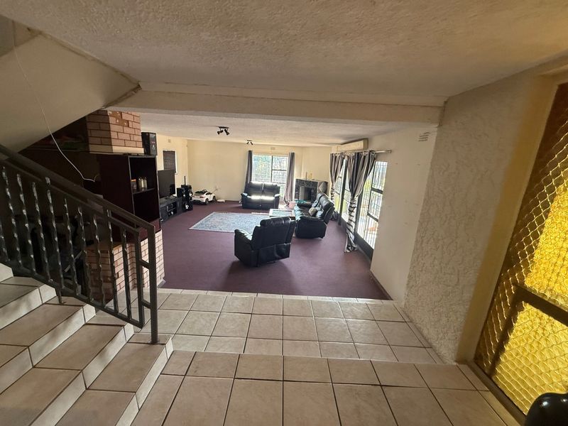 Spacious living area featuring a brick fireplace, split-level flooring with tiles and carpet, and direct access to the staircase.