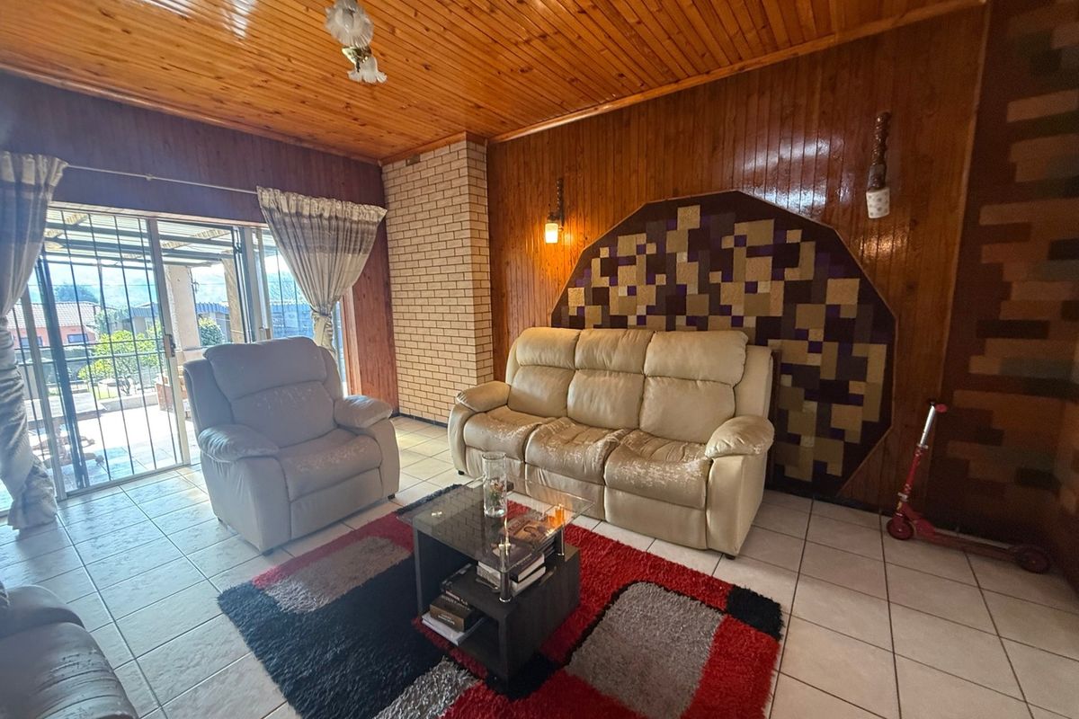 Living room featuring wood-panelled walls and ceiling, tiled flooring, and a brick feature wall with access to an outdoor patio area.