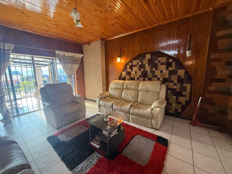 Living room featuring wood-panelled walls and ceiling, tiled flooring, and a brick feature wall with access to an outdoor patio area.