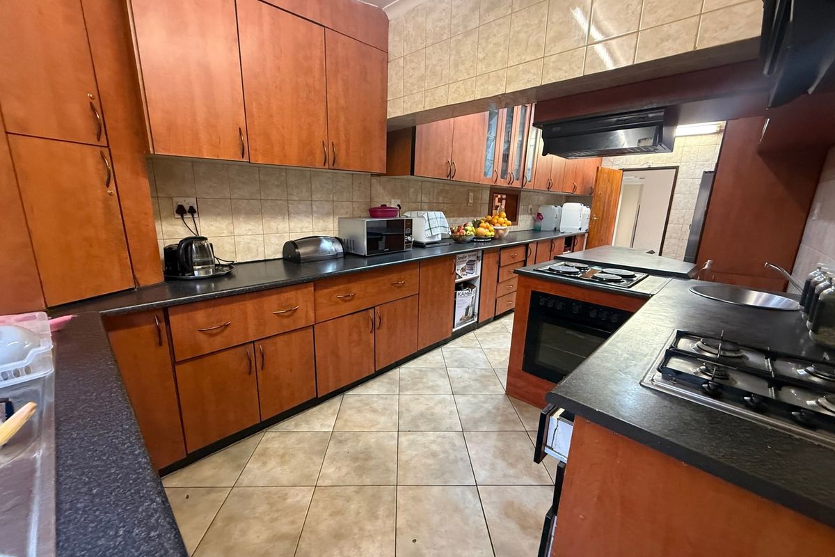 A functional kitchen featuring extensive wood-look cabinetry, dark laminate countertops, ceramic tile flooring, and built-in cooking appliances including a gas hob and oven.