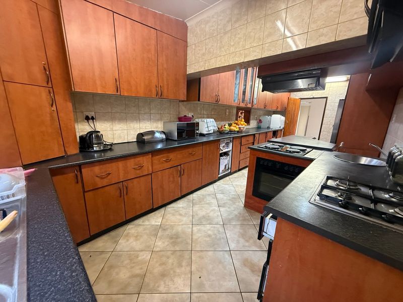 A functional kitchen featuring extensive wood-look cabinetry, dark laminate countertops, ceramic tile flooring, and built-in cooking appliances including a gas hob and oven.