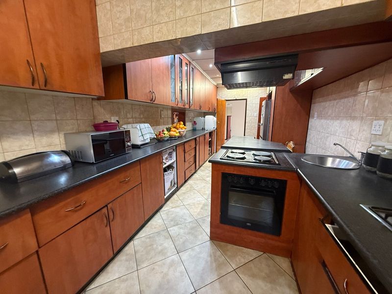 A functional kitchen featuring wooden cabinetry, dark countertops, a built-in oven with hob, and tiled finishes throughout.