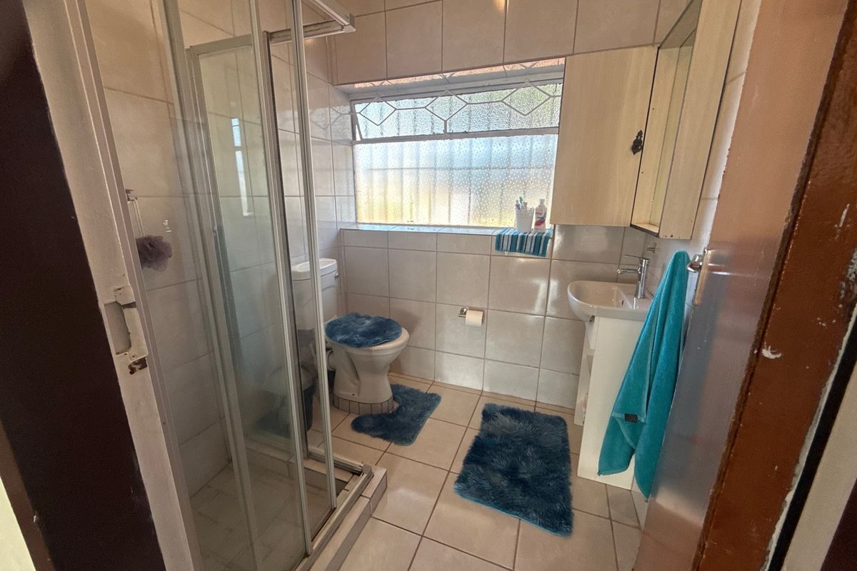 A functional bathroom featuring a shower enclosure, pedestal basin, and toilet with tiled finishes throughout.