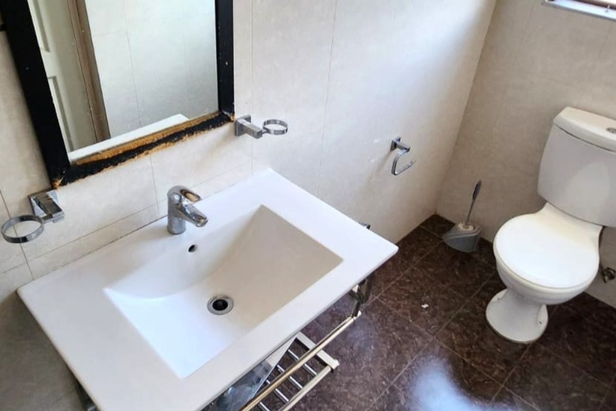 A functional bathroom featuring a wall-mounted vanity basin, chrome fixtures, and a standard toilet with tiled finishes throughout.