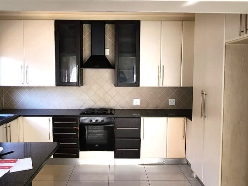 A functional kitchen featuring two-tone cabinetry, granite countertops, a built-in oven with gas hob, and a double basin sink.