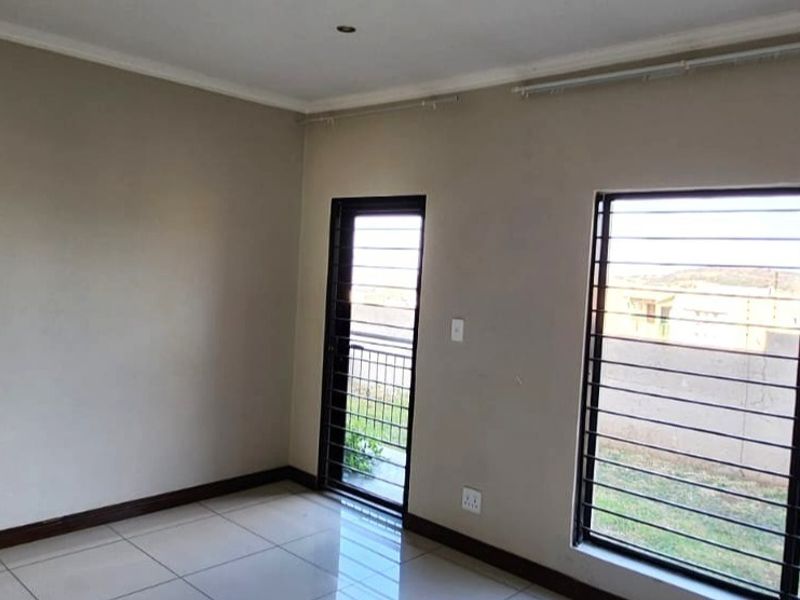 A bright, empty bedroom featuring tiled flooring, security bars on the windows and door, and neutral wall finishes.
