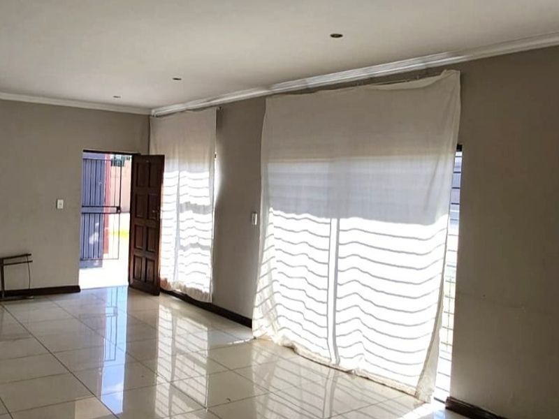 A spacious, empty living area featuring neutral tiled flooring, recessed lighting, and large sliding glass doors leading to an exterior entrance.