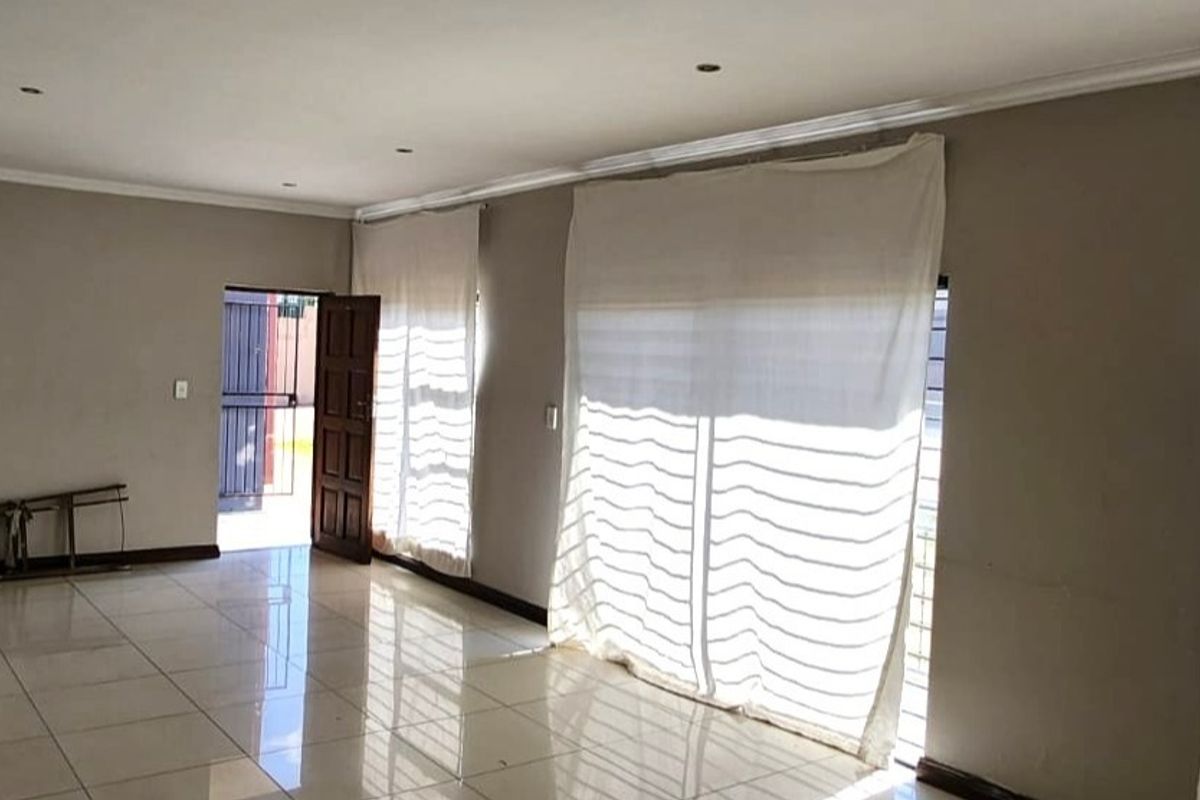 A spacious, empty living area featuring neutral tiled flooring, recessed lighting, and large sliding glass doors leading to an exterior entrance.