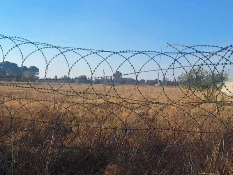A view of the property's open land perimeter, secured with heavy-duty razor wire fencing.