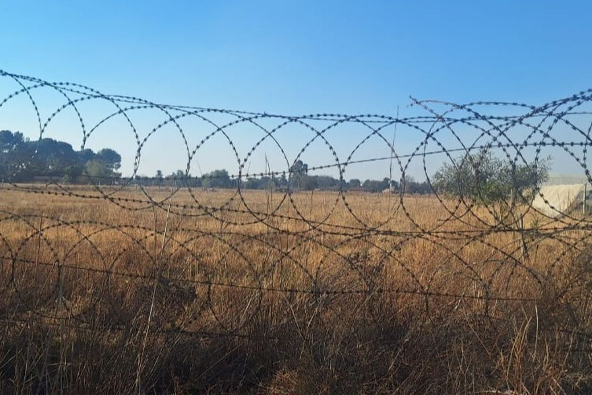 A view of the property's open land perimeter, secured with heavy-duty razor wire fencing.