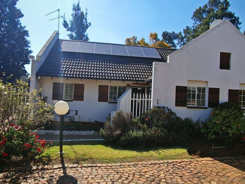 Front elevation of a townhouse featuring a tiled roof with solar panels, cobblestone driveway, and secure gated entrance with window shutters.