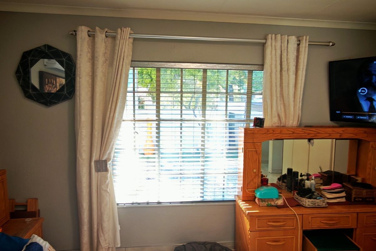 A bedroom featuring a window with security bars and neutral wall finishes, providing a functional space with natural light.