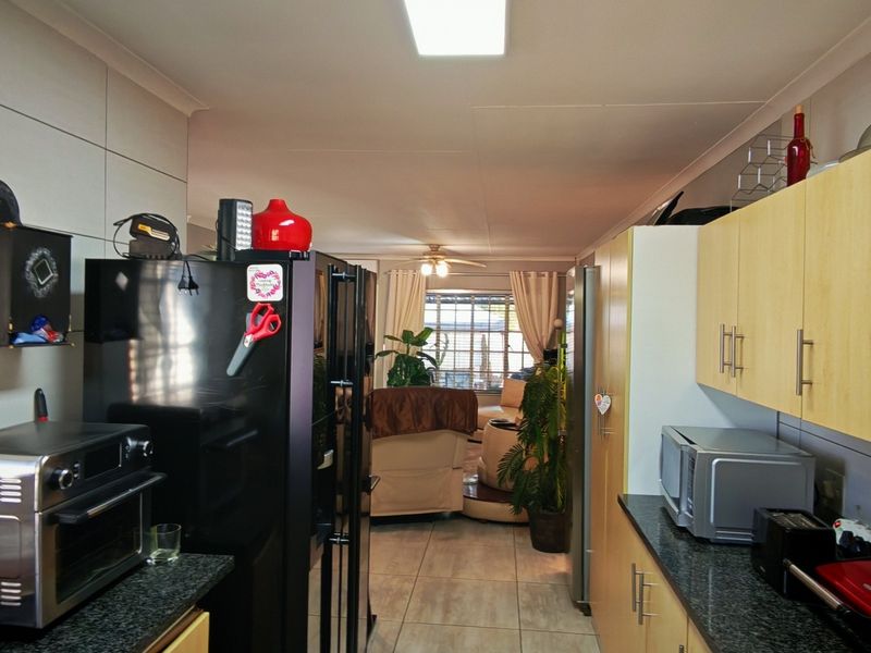 A functional kitchen featuring granite countertops, light-toned cabinetry, and tiled flooring, leading into an open-plan living area.