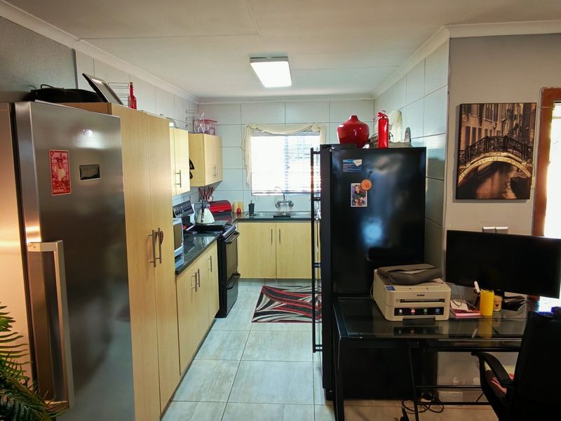 A functional kitchen featuring light wood-finish cabinetry, tiled flooring, and a tiled backsplash, providing a practical workspace with integrated appliances.