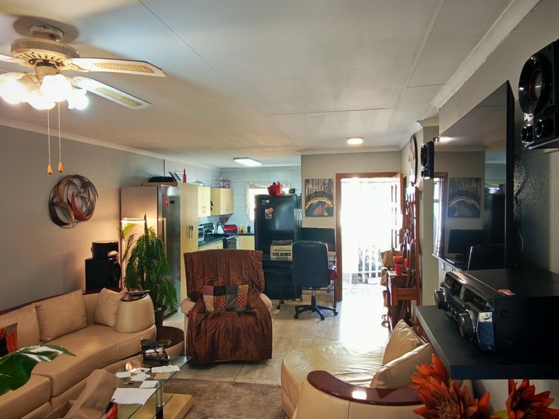 Open plan living area featuring tiled flooring and a ceiling fan, seamlessly connecting to the kitchen space with built-in cabinetry.