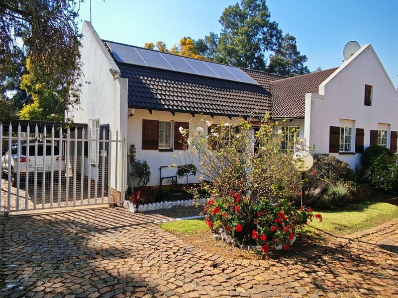 Front elevation of a townhouse featuring a cobblestone driveway, security gate, and roof-mounted solar panels.