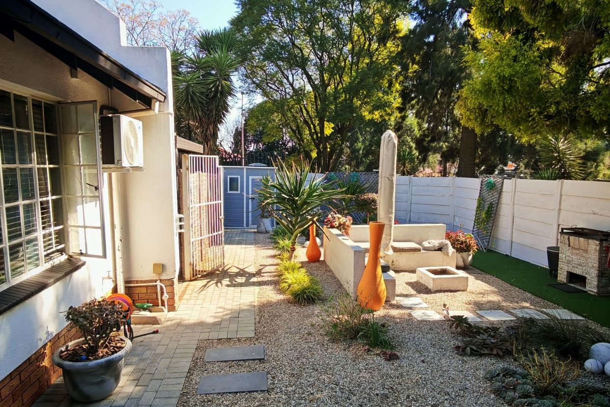 A rear garden area featuring a paved walkway, gravel landscaping, a built-in braai, and a precast concrete boundary wall.